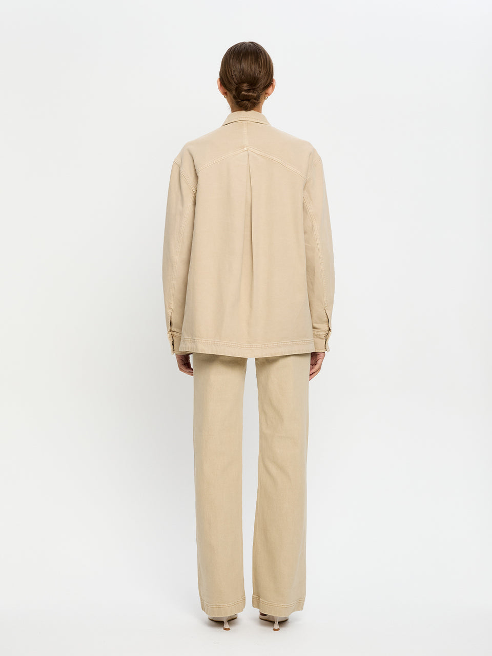 Woman wearing a beige denim shirt and jeans on a white background