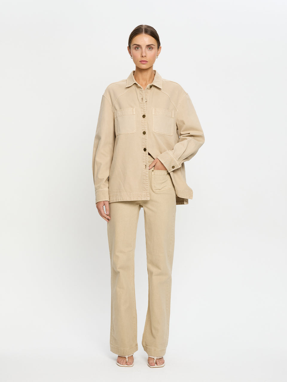 Woman wearing a beige denim shirt and jeans on a white background