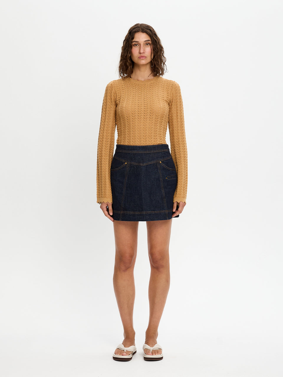 Woman wearing a mustard yellow top and dark denim skirt on a white background
