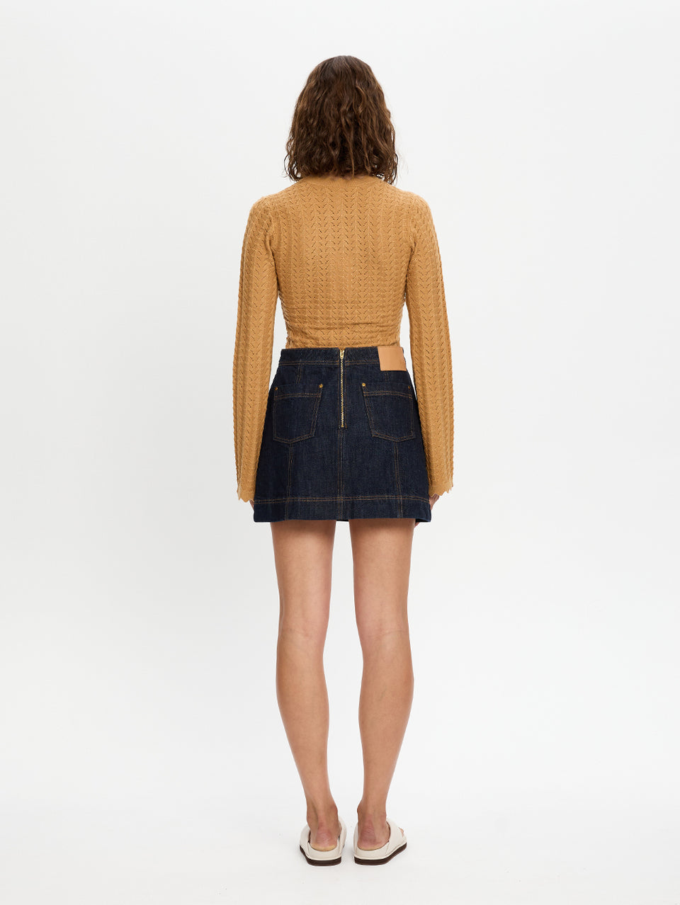 Woman wearing a mustard yellow textured top and dark denim skirt on a white background