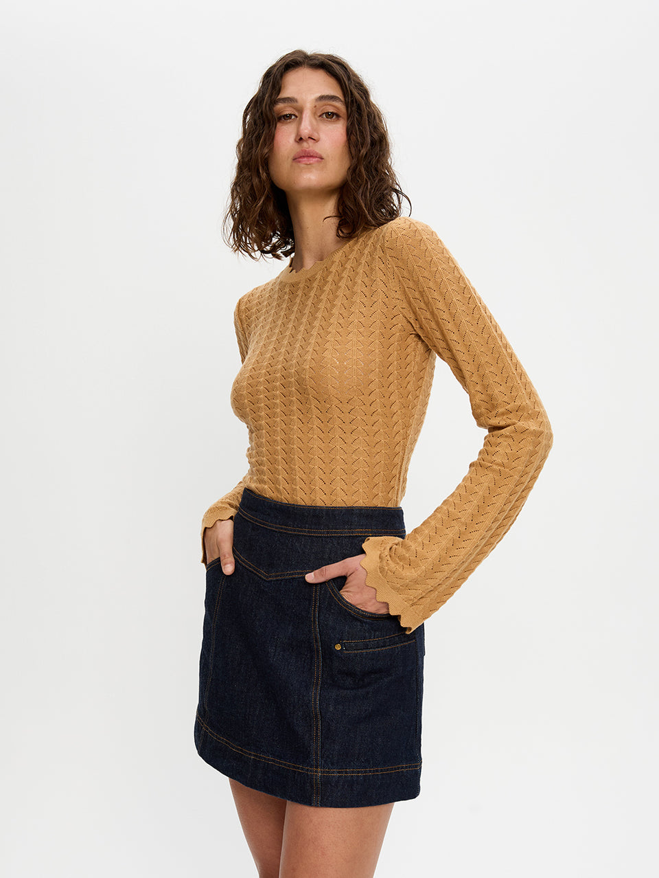 Woman wearing a mustard yellow sweater and dark denim skirt on a white background