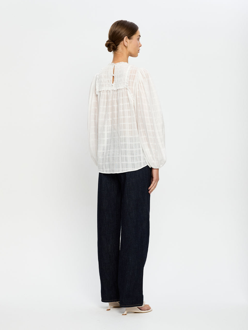 Woman wearing a white blouse and dark pants on a white background