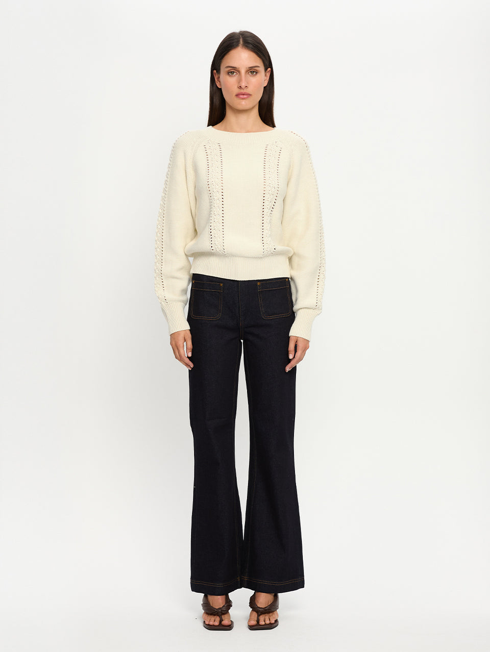 Woman wearing a cream sweater and black pants on a white background