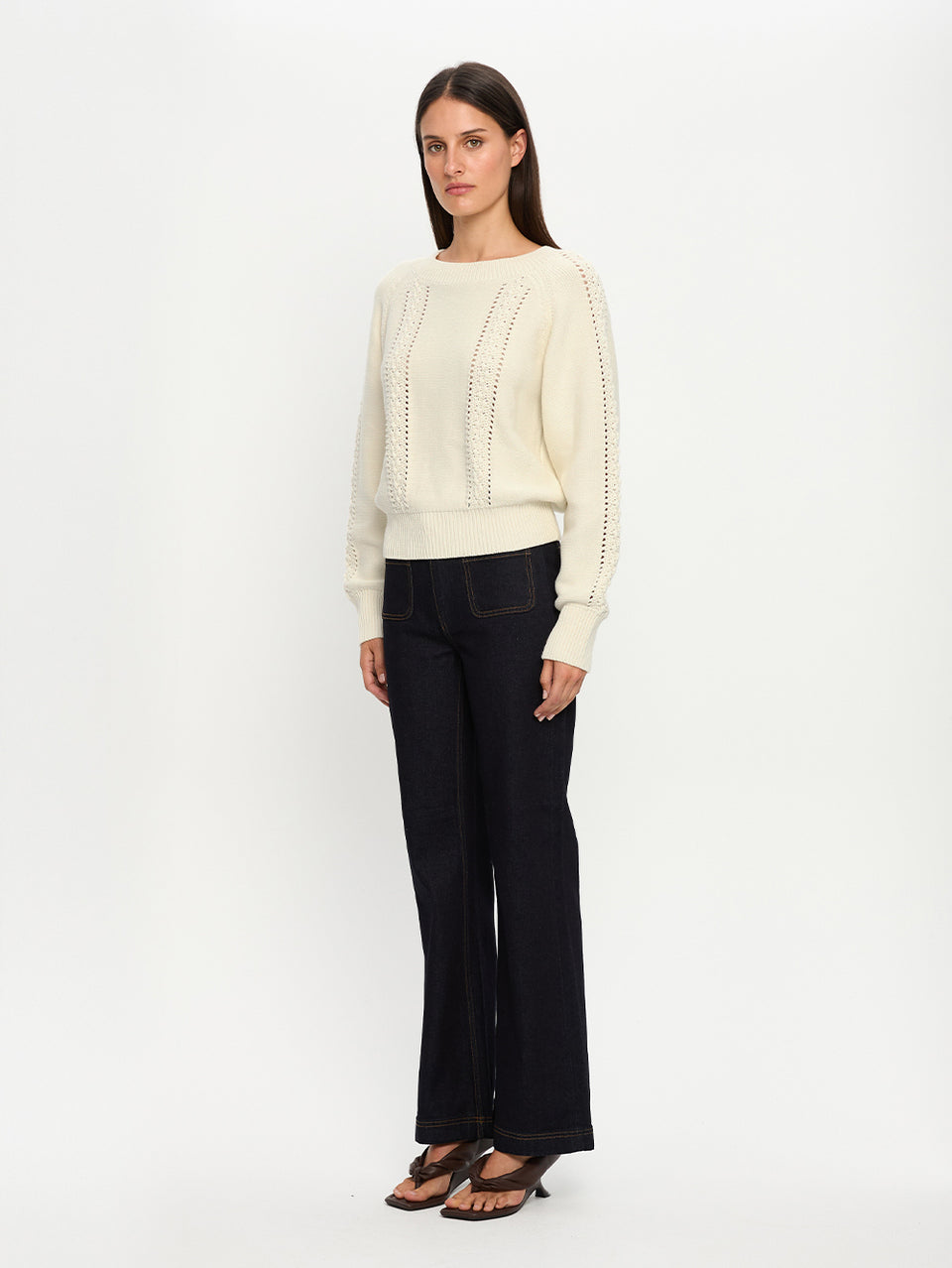 Woman wearing a cream sweater and black pants on a white background