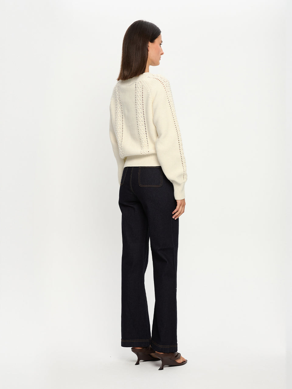 Woman wearing a cream sweater and black pants on a white background
