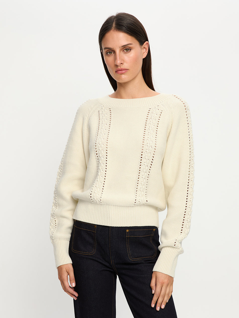 Woman wearing a cream sweater with lace details on a white background