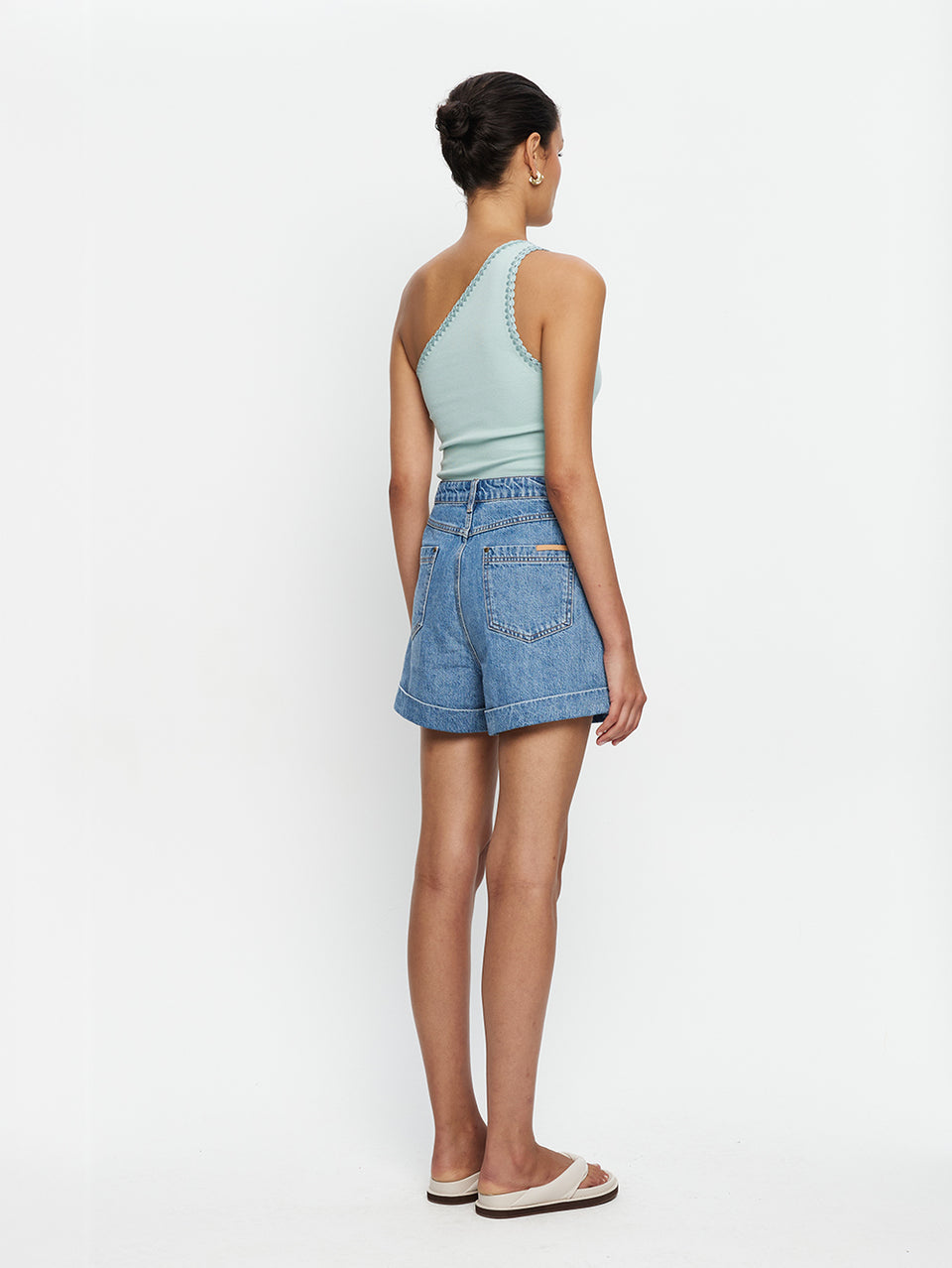 Woman wearing a light blue halter top and denim shorts on a white background