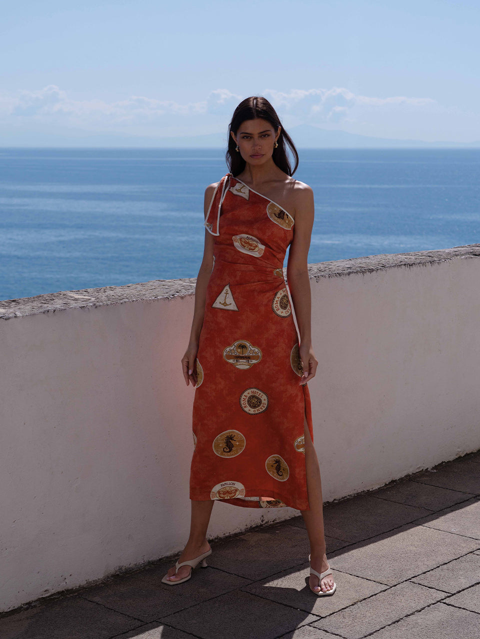 Woman in a red dress with stamp patterns standing on a rooftop with ocean view