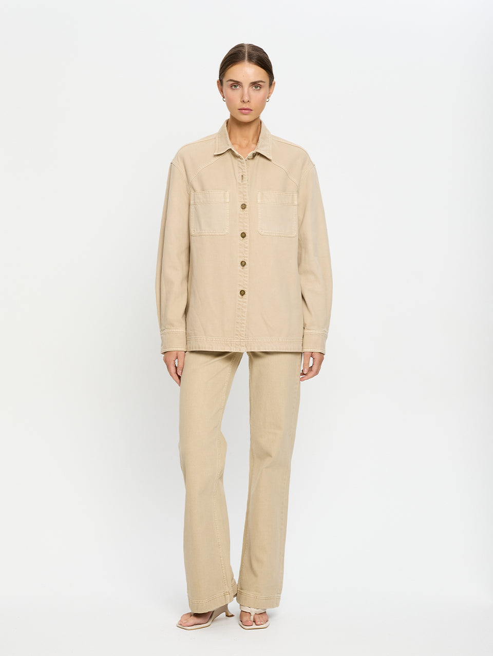 Woman wearing a beige denim shirt and jeans on a white background