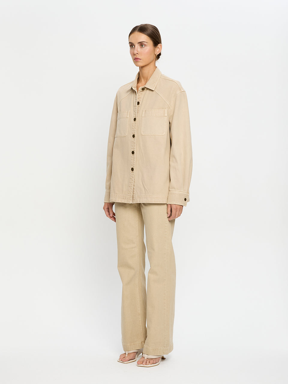 Woman wearing a beige denim shirt and jeans on a white background