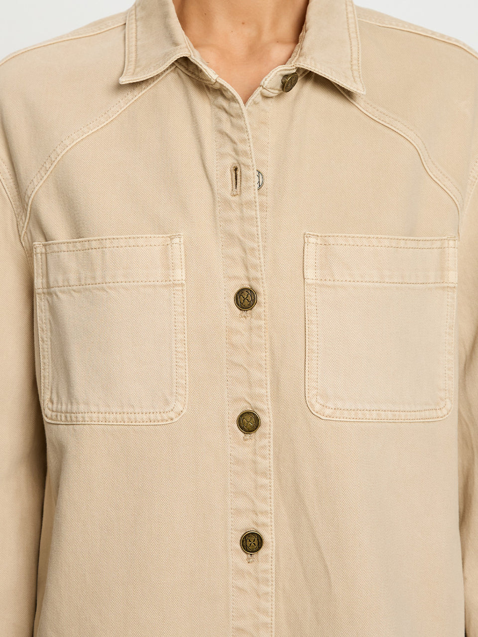 Beige button-up shirt with two front pockets on a plain background