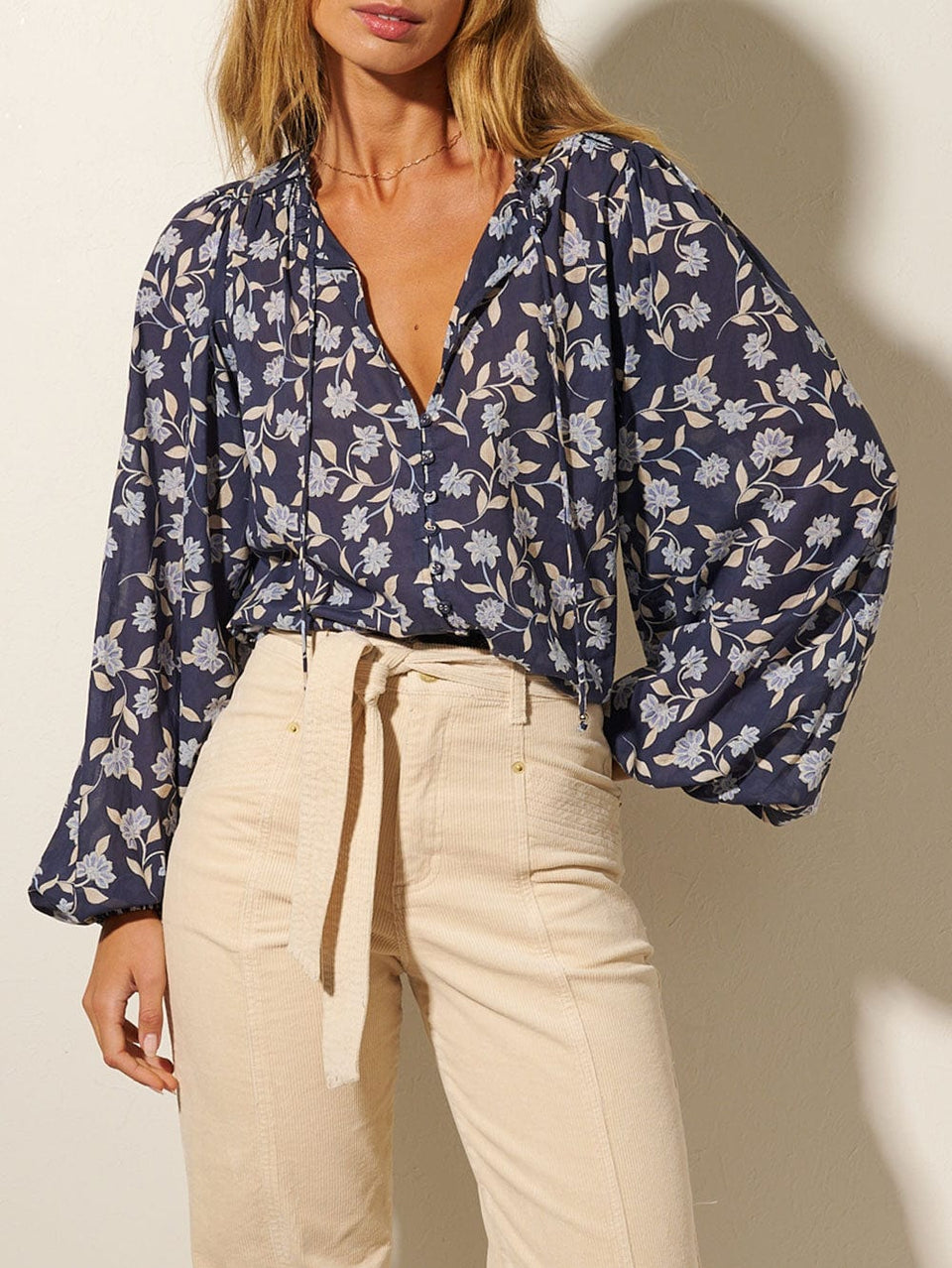 Studio model wears KIVARI Jeanne Blouse: A navy and sky blue floral blouse made from cotton and featuring a button front, full-length blouson sleeves and frill collar detail.