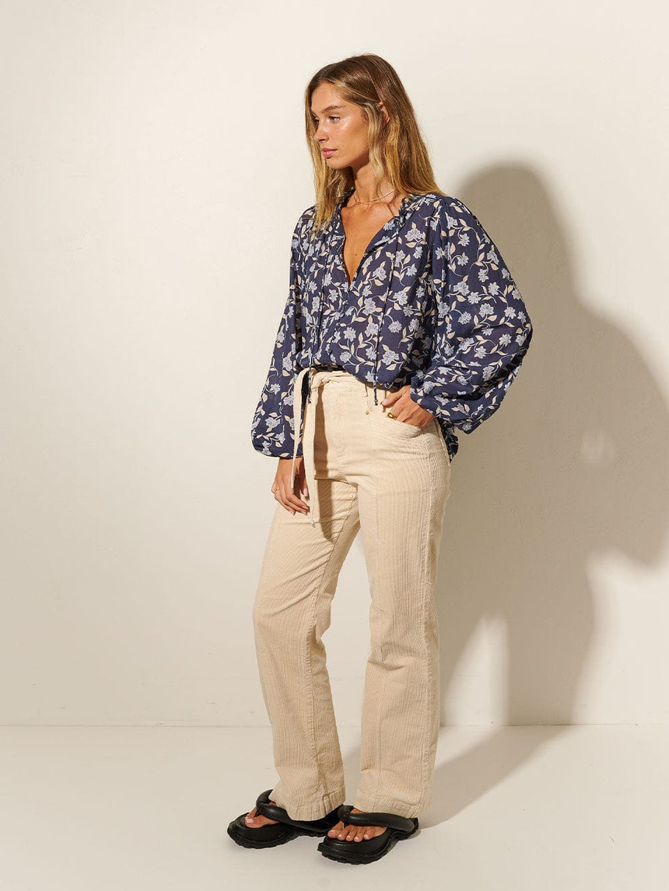 Studio model wears KIVARI Jeanne Blouse: A navy and sky blue floral blouse made from cotton and featuring a button front, full-length blouson sleeves and frill collar detail.