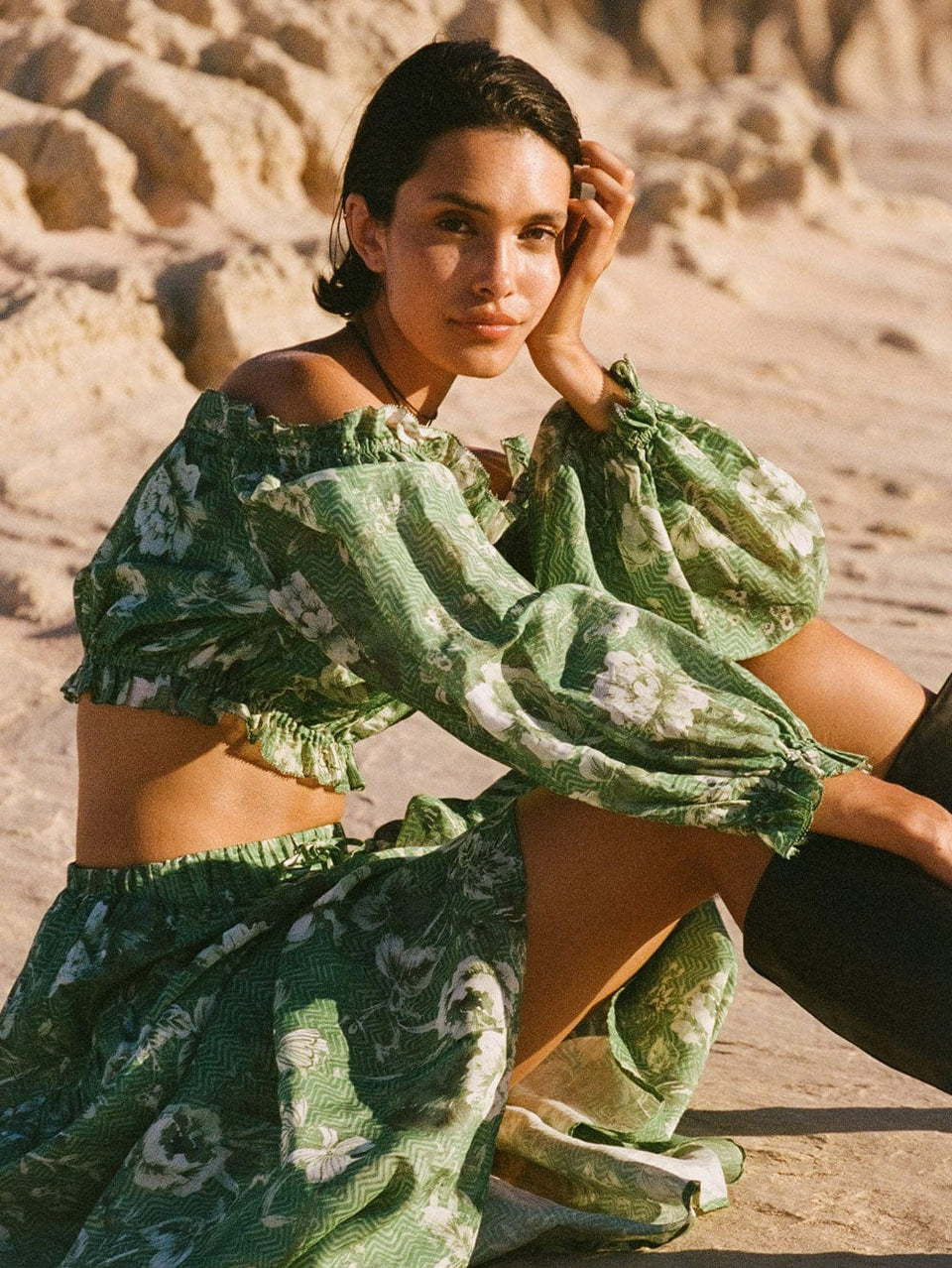 Campaign model wears KIVARI Khalo Crop Top: A green floral off-the-shoulder top with full-length blouson sleeves and elasticated bust, waist and sleeve details.