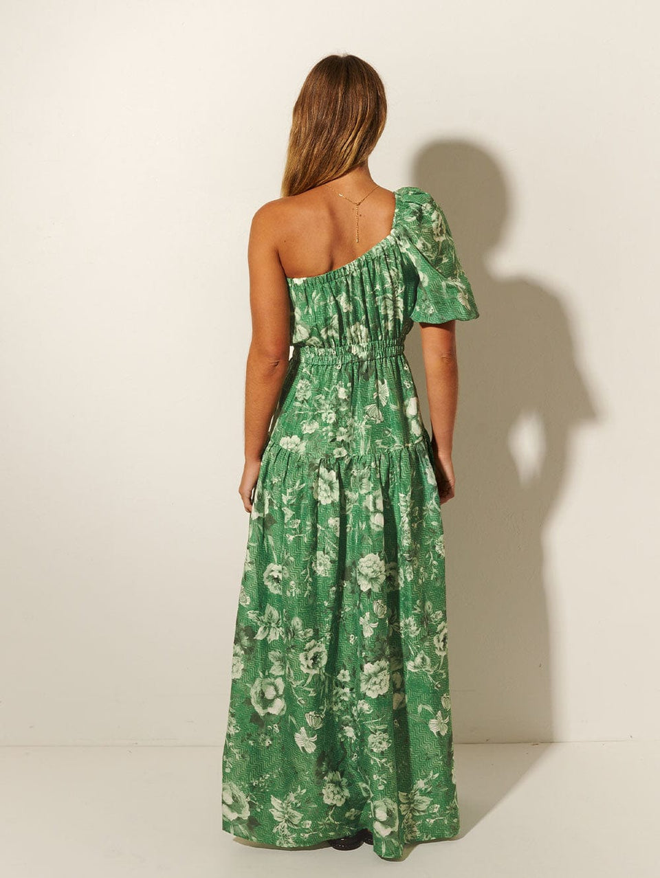 Studio model wears KIVARI Khalo Maxi Dress: A green floral one-shoulder dress with a short sleeve, elasticated front and waist, and tiered skirt.