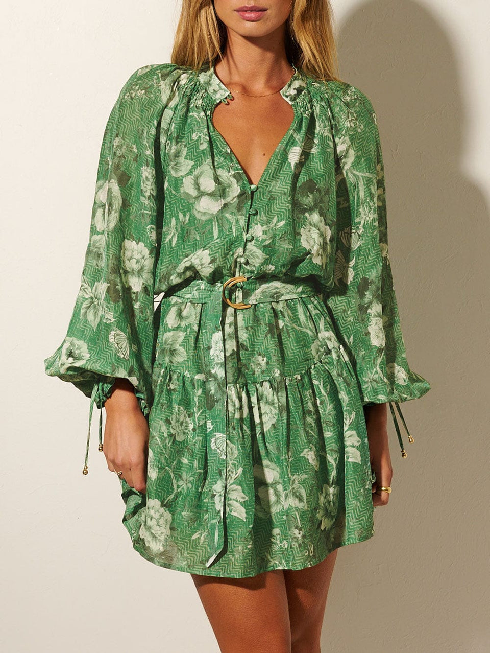 Studio model wears KIVARI Khalo Mini Dress: A green floral dress featuring a button-through bodice, full-length blouson sleeves and a tiered skirt with belt. 
