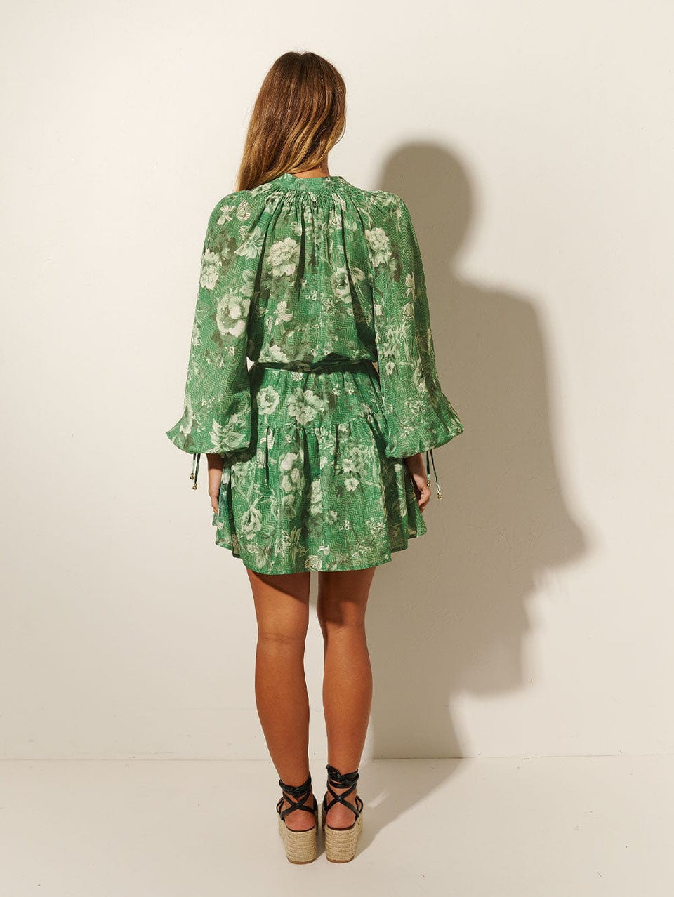 Studio model wears KIVARI Khalo Mini Dress: A green floral dress featuring a button-through bodice, full-length blouson sleeves and a tiered skirt with belt. 
