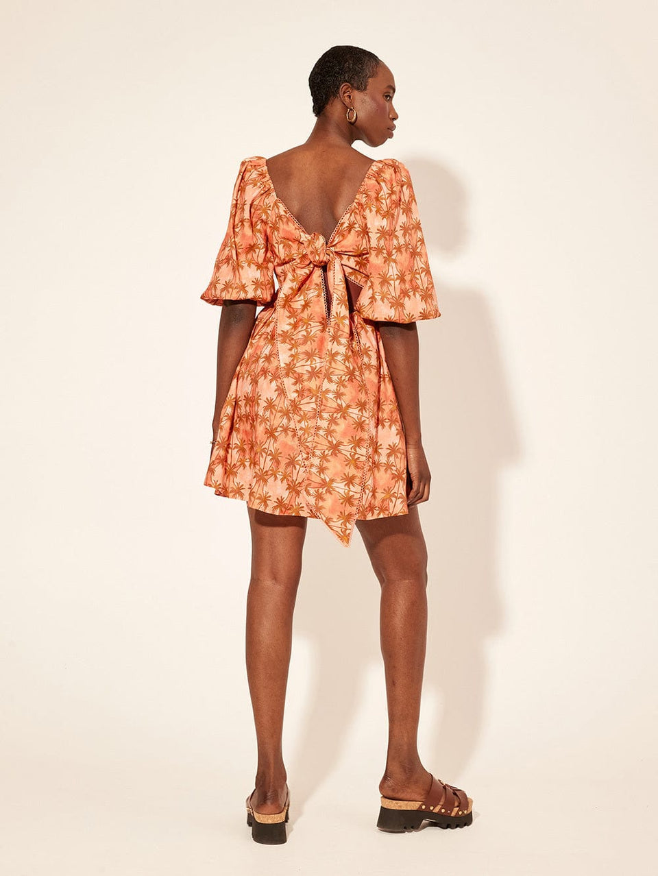 Leilani Mini Dress KIVARI | Model wears bronze and peach palm printed mini dress back view