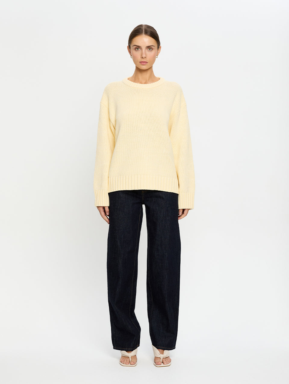 Woman wearing a light yellow sweater and navy pants on a white background