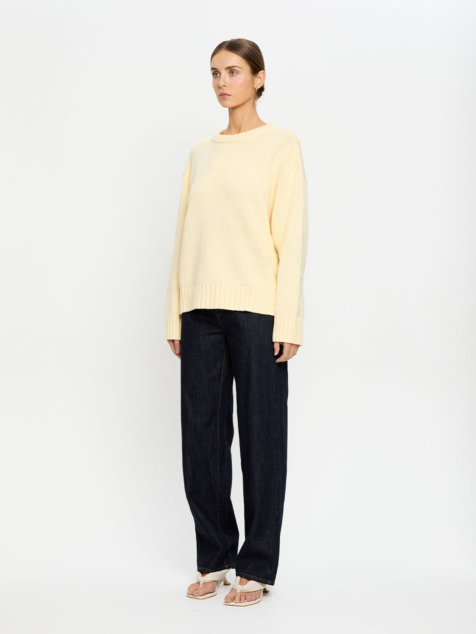 Woman wearing a light yellow sweater and navy pants on a white background