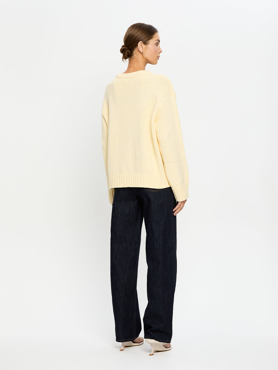 Woman wearing a light yellow sweater and dark blue jeans on a white background