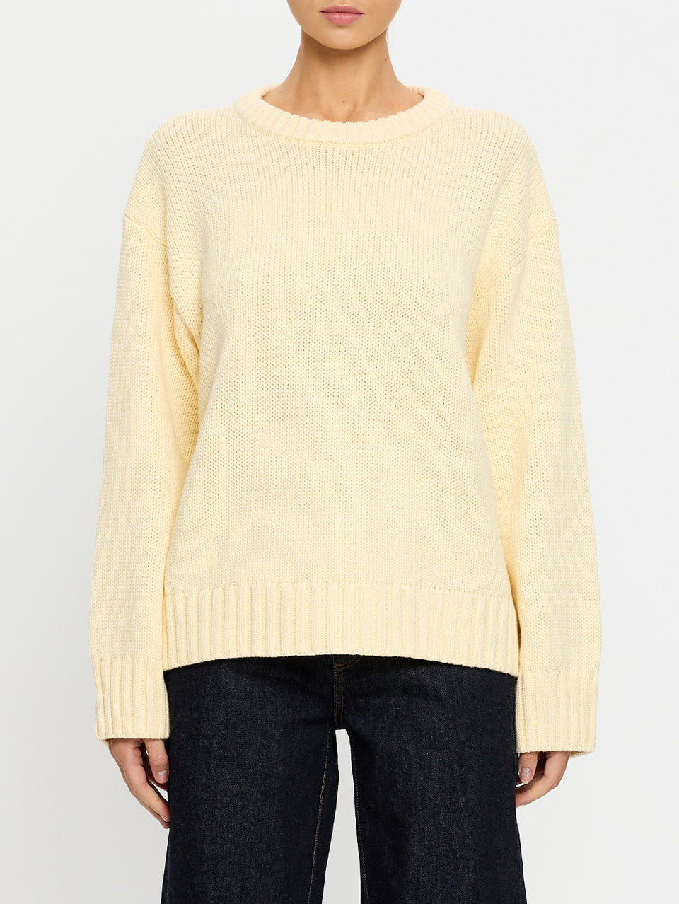 Person wearing a light yellow sweater and dark jeans on a white background