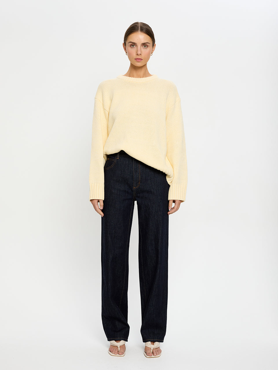 Woman wearing a yellow sweater and navy jeans on a white background