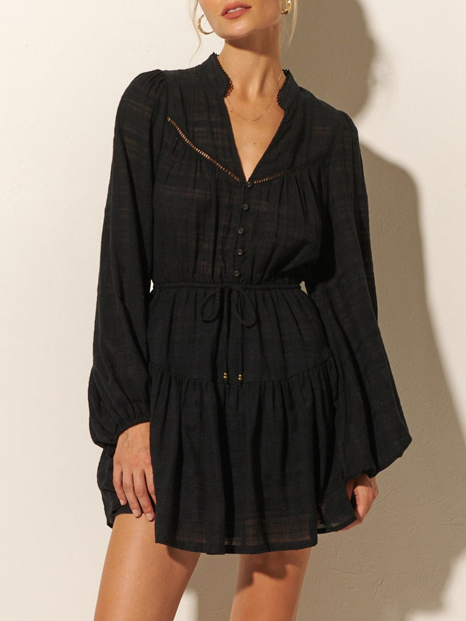 Close-up: Studio model wears the KIVARI Rafaelle Mini Dress: a black dress made from cotton check featuring a button-front bodice, full-length blouson sleeves, drawstring waist and gathered hem frill.