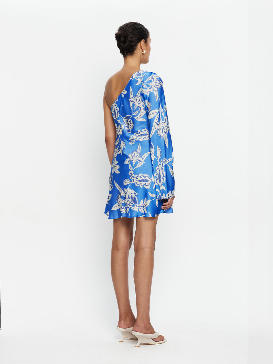 Woman wearing a blue floral one-shoulder dress on a white background