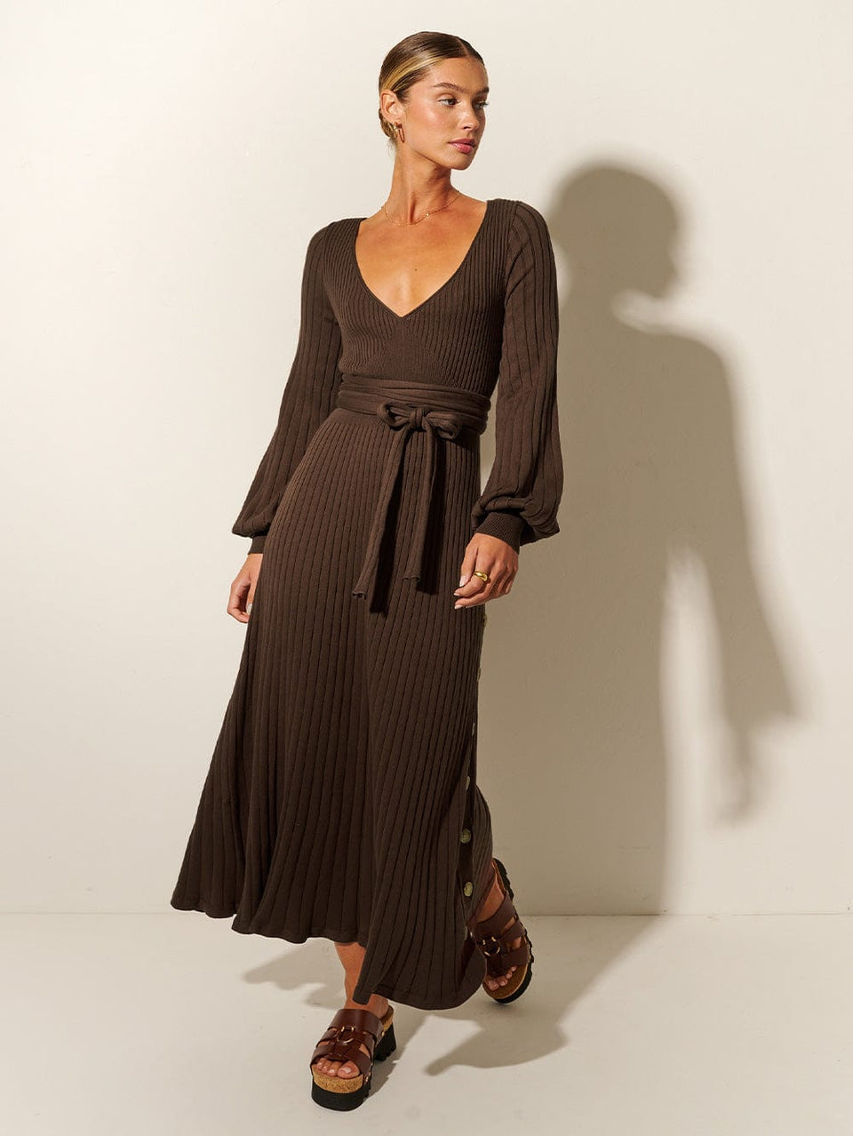 Studio model wears the KIVARI Yolanda Long Sleeve Knit Dress - Chocolate: A rich brown reversible dress made from rib knit stitching with soft underbust seams, a tie-back feature with cut-out detail, full-length blouson sleeves and an A-line skirt.
