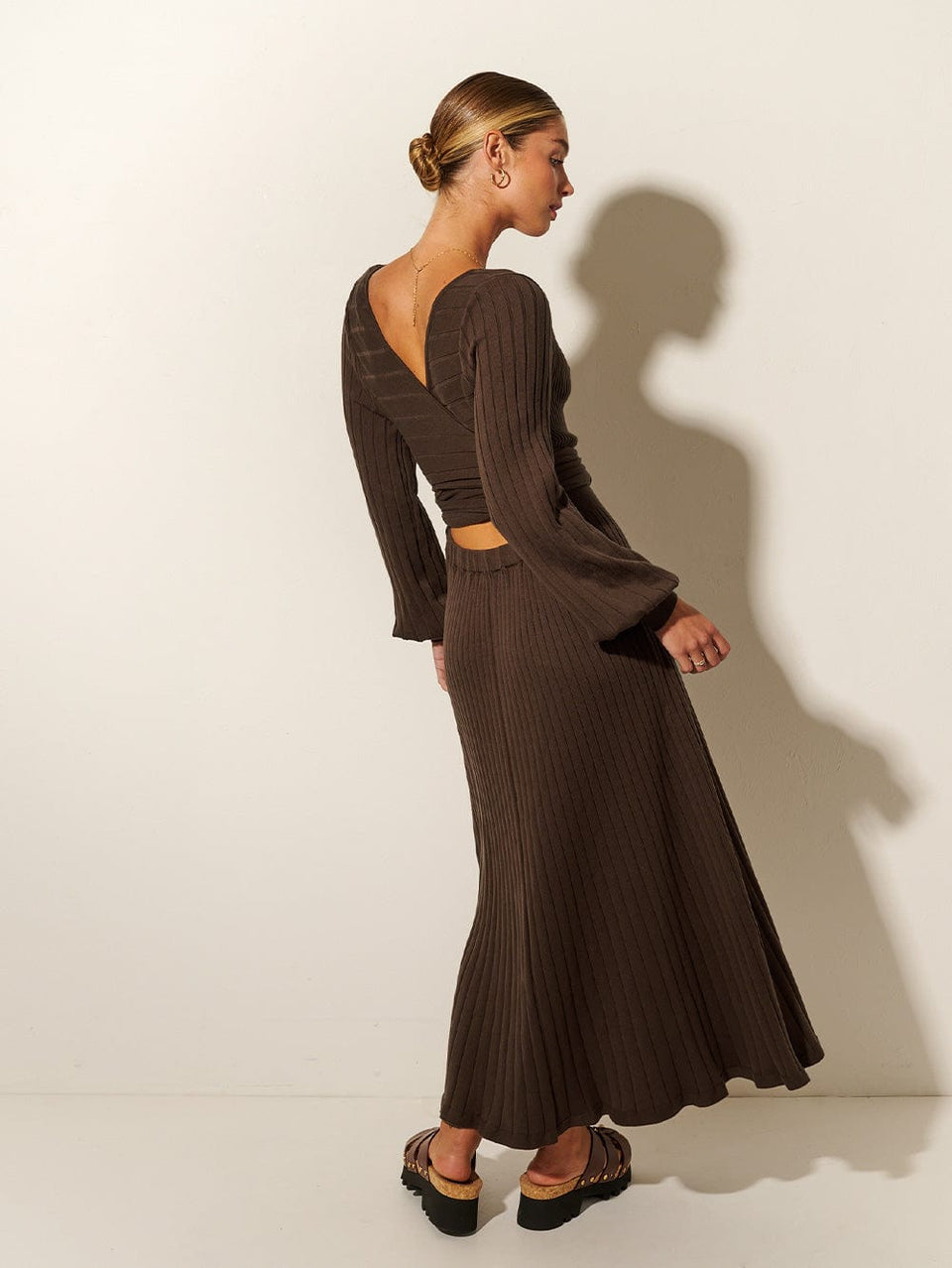 Studio model wears the KIVARI Yolanda Long Sleeve Knit Dress - Chocolate: A rich brown reversible dress made from rib knit stitching with soft underbust seams, a tie-back feature with cut-out detail, full-length blouson sleeves and an A-line skirt.
